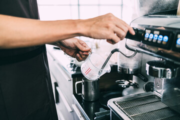 Close-up barista hands steaming on a coffee beaker with a coffee machine with high temperature for making cappuccino or latte coffee in a coffee shop.