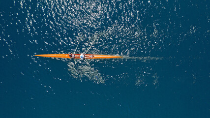 Aerial drone top down view of sport canoe operated by team of young trained athletes in deep blue...