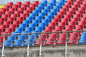 The stands of an Italian football stadium without fans. Empty red and blue plastic chairs. Empty stadium