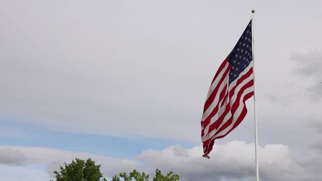  Large american flag flying in slow motion on a windy day over thick white clouds.