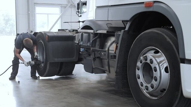 A professional mechanic uses a pneumatic wrench to screw in a lorry rear axle wheel nut at a truck service station