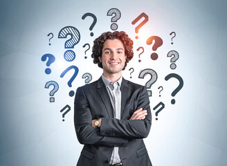 Portrait of hispanic handsome young businessman in suit with crossed arms pose and wondering about career opportunities. Question marks drawn on wall behind. Concept of searching for an answer.