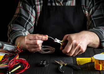 Professional master electrician cuts white wire with diagonal pliers. Working environment on the workshop table