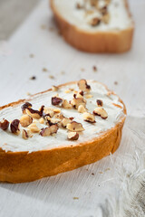 Soft cheese sandwich sprinkled with nuts on a white wooden table.