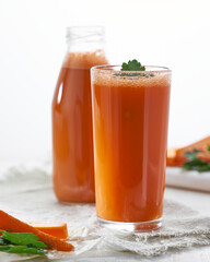Carrot juice in bottle and a glass and slices of fresh fruit isolated on white background.