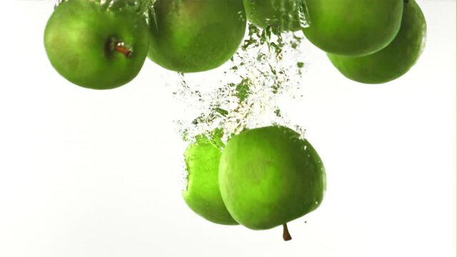 Super slow motion whole green apples fall under the water with air bubbles. On a white background. Filmed on a high-speed camera at 1000 fps. High quality FullHD footage