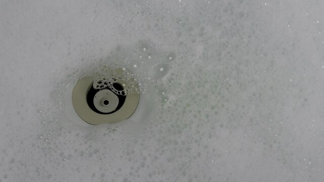 Close up of bathtub. Emptying a bathtub with bubbles. The water flows down in a vortex down the drain. The bath foam runs down last and fills the drain.