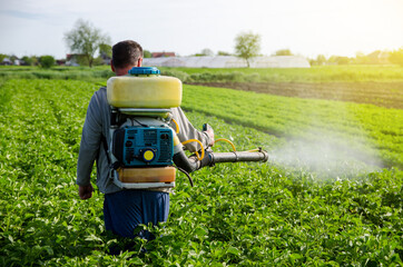 A farmer with a mist fogger sprayer sprays fungicide and pesticide on potato bushes. Effective crop...