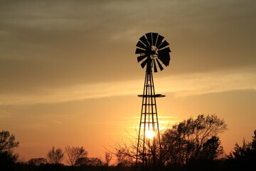 Kansas sunset with a Windmill with clouds and tree silhouette's that's bright and colorful out in the country north of Hutchinson Kansas USA.