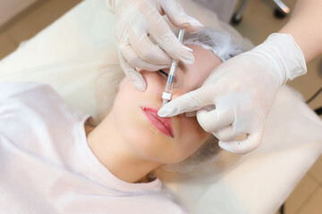 The girl is undergoing a lip augmentation procedure with a master cosmetologist who holds the lip...