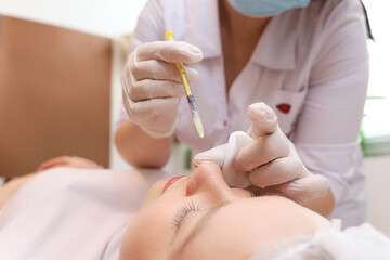 The cosmetologist leaning over the client performs a chin lift procedure by injection cosmetic injections