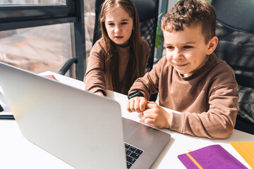 Little boy and girl study online in home at the laptop