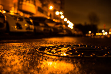 Rainy night in the big city, the light from the lanterns in the courtyard of the house in which the parked cars. View from the hatch at the level of the pavement