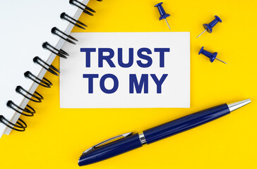 On a yellow background lies a notebook, a pen and a business card with the inscription - Trust to My