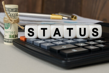 There are cubes on the calculator that say - STATUS. Nearby out of focus - dollars, notebook and pen