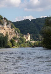 Fototapeta na wymiar Canoeing and tourist boat, in French called gabare, on the river Dordogne at La Roque-Gageac and Chateau La Malartrie in the background. Aquitaine, France