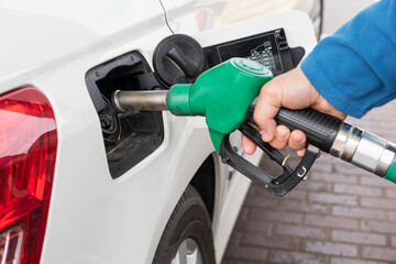 Man's hand holds a refueling hose near the hatch of a gas tank of a car and prepares to refuel the car with gas