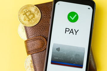 Application for payment on the smartphone screen on the wallet with bitcoins on the yellow background.