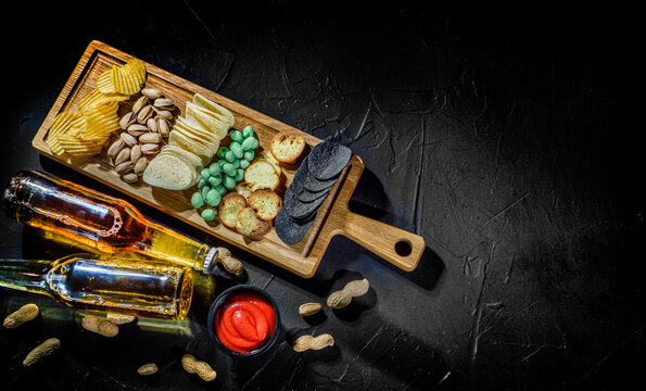 Cold beer with potato chips, snacks and sauce on dark background. Top view with space for text