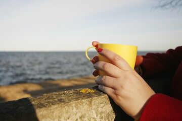 Yellow mug with tea in the hands of woman
