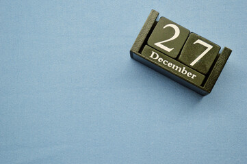 Wooden calendar from blocks on a blue background with copy space. December 27th
