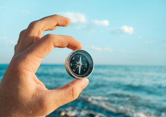 Compass in the hand of a male tourist in the background blue sea and sky.
