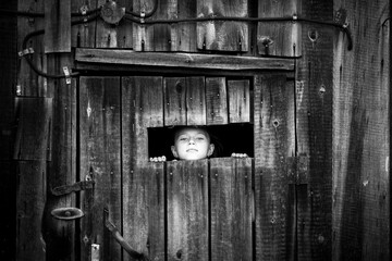 Little girl looks out of the shed through a small window.