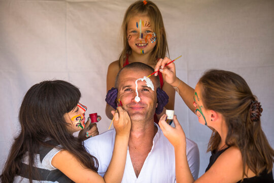 Children girls paints face of his father. Happy family.