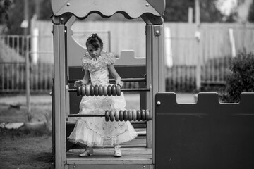 Little cute girl in an elegant dress on the child playground. Black and white photo.
