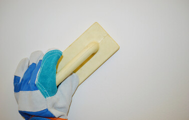 Hand in blue work cloth glove hold construction wooden trowel against white wall