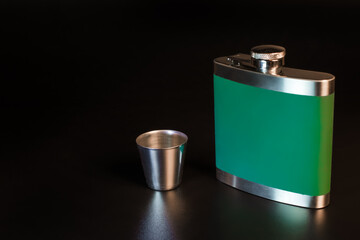 Green flask for alcohol and an iron shot glass on a black background
