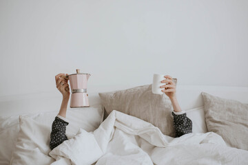 good morning: a geyser coffee maker, a glass and female hands from under the blanket, funny concept 