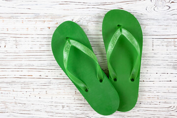 green rubber flip-flops on a white wooden background, view from above