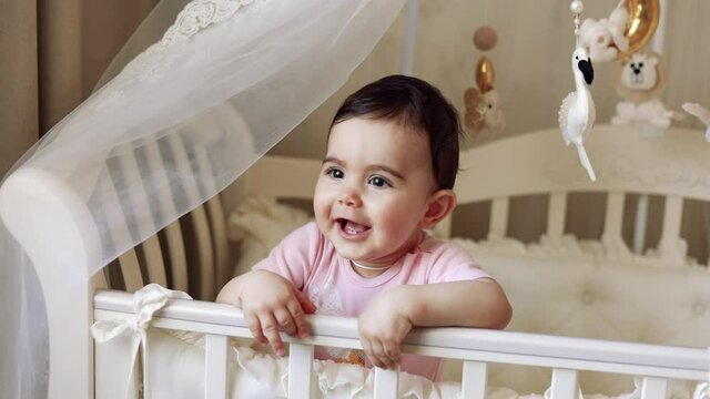 Cute baby 9 months laughing in a cot in the room of the house.High quality 4k footage