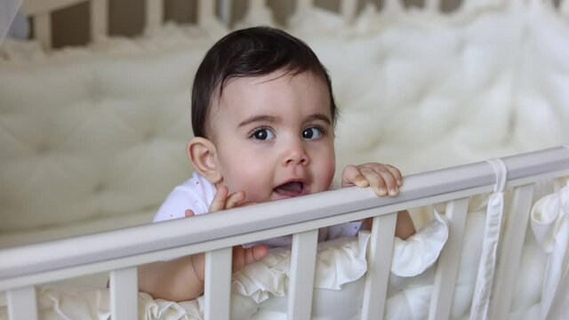 Cute baby 9 months laughing in a cot in the room of the house.High quality 4k footage