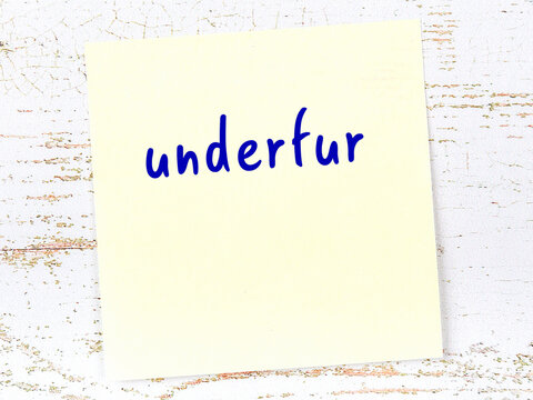 Yellow sticky note on wooden wall with handwritten word underfur