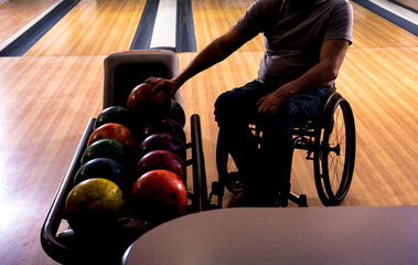 Young disabled man in wheelchair playing bowling in the club