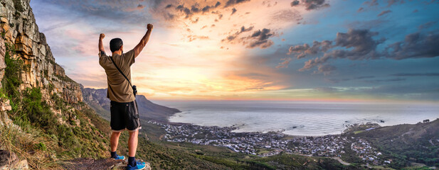 Victory and success after a hike up Table Mountain at sunset. Looking over the bay with colourful enhanced sunset - Great outdoors adventure and travel holiday destination, Cape Town, South Africa - obrazy, fototapety, plakaty