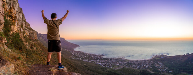 Victory and success after a hike up Table Mountain at sunset with clear skies looking over the bay  - Great outdoors adventure and travel holiday destination, Cape Town, South Africa - obrazy, fototapety, plakaty