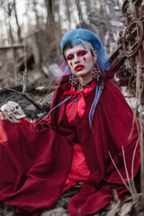 Obraz premium Beautiful gothic model with a skull in her hands. A girl with blue hair sits at the cross. Bright red gothic makeup.
