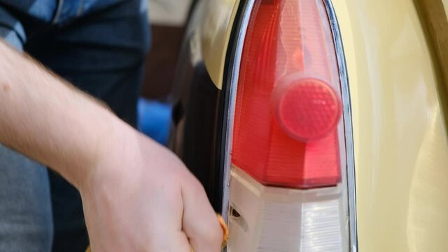 Polishing the chrome surround of red rear light and reversing, on beige burgundy retro car.