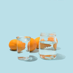 Creative visual idea, fresh oranges seen through glass and jar filled with water on pastel blue background. Modern minimal concept.