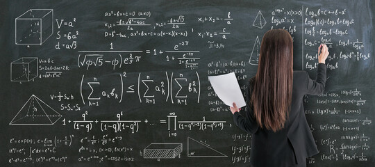 Education and studying concept with back view on girl student writing on chalkboard calculations...