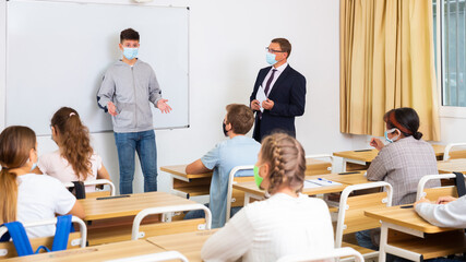 Schoolboy in protective mask is standing near whiteboard and answer about task in the classroom