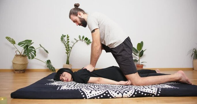 Mixed race latin woman having massage at home. Bearded man making yoga thai massage trigger point work shiatsu physical therapy fascia release