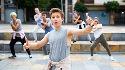 Happy positive teenagers learn dance movements at city street