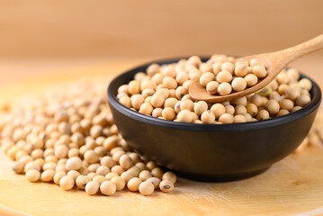 Soybean seeds in black bowl with spoon on wooden background