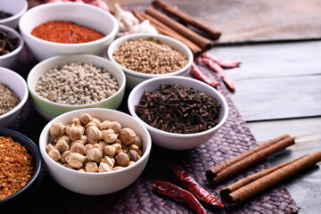 Various dry spices and herbs in a bowl on wooden background. Asian food ingredients (chili, clove, caraway, coriander seed, star anise, cardamom, pepper, cinnamon, garlic and shallot)