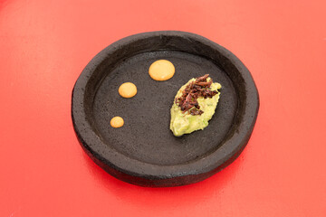 Beautiful black stone plate with points of salsa and guacamole topped with red grasshoppers