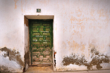 Front View Closed Antique Wooden Door Painted Green On A White Wall With Obvious Signs Of Abandonment